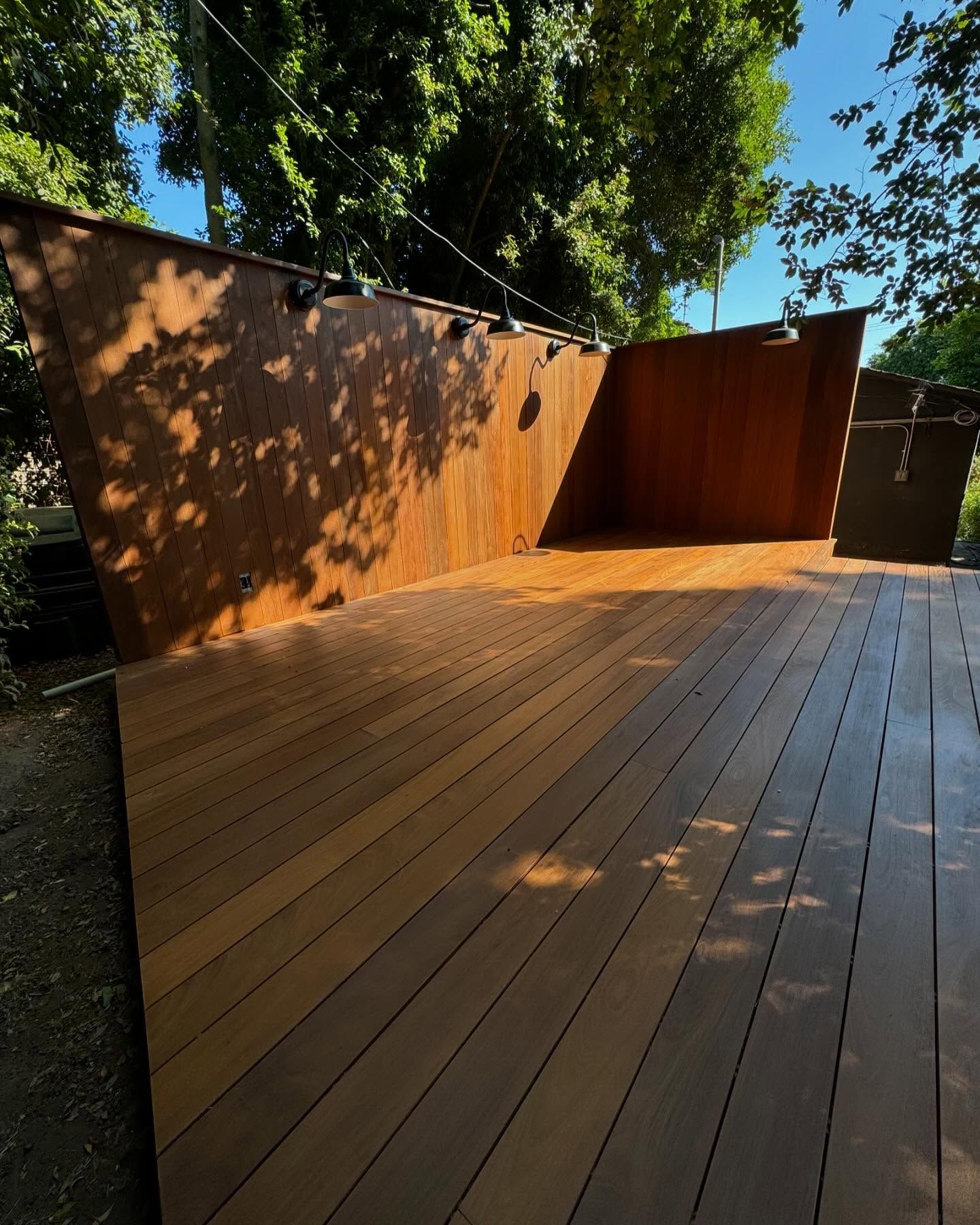 Wooden deck with rusted metal walls in a wooded area. Sunlight casts shadows.