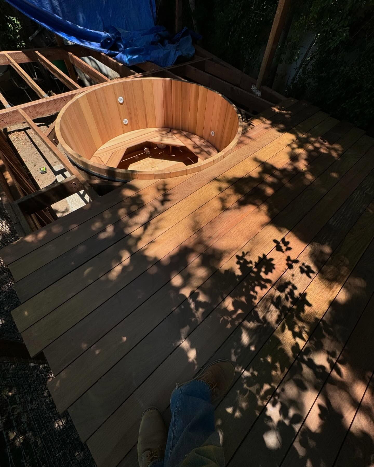 Wooden hot tub installed on a deck, with visible tree shadows.