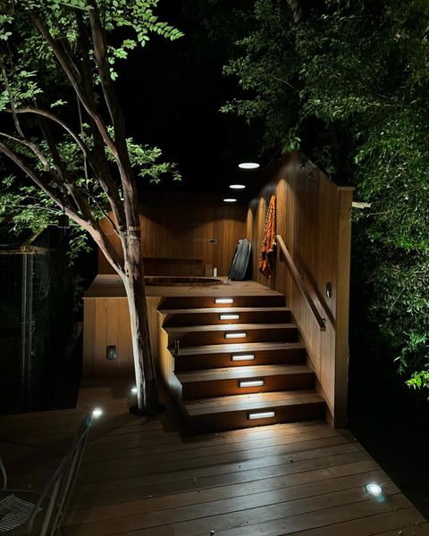 Wooden staircase lit by lights at night, leading to a deck with trees.