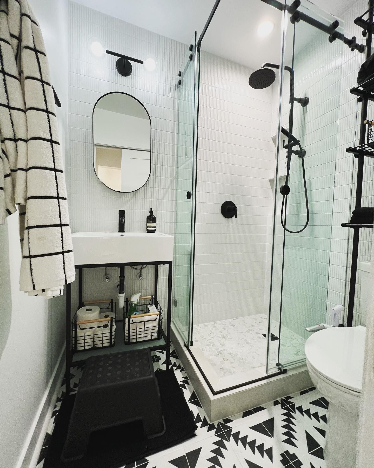 Small, modern bathroom with black and white decor, shower, sink, and toilet.