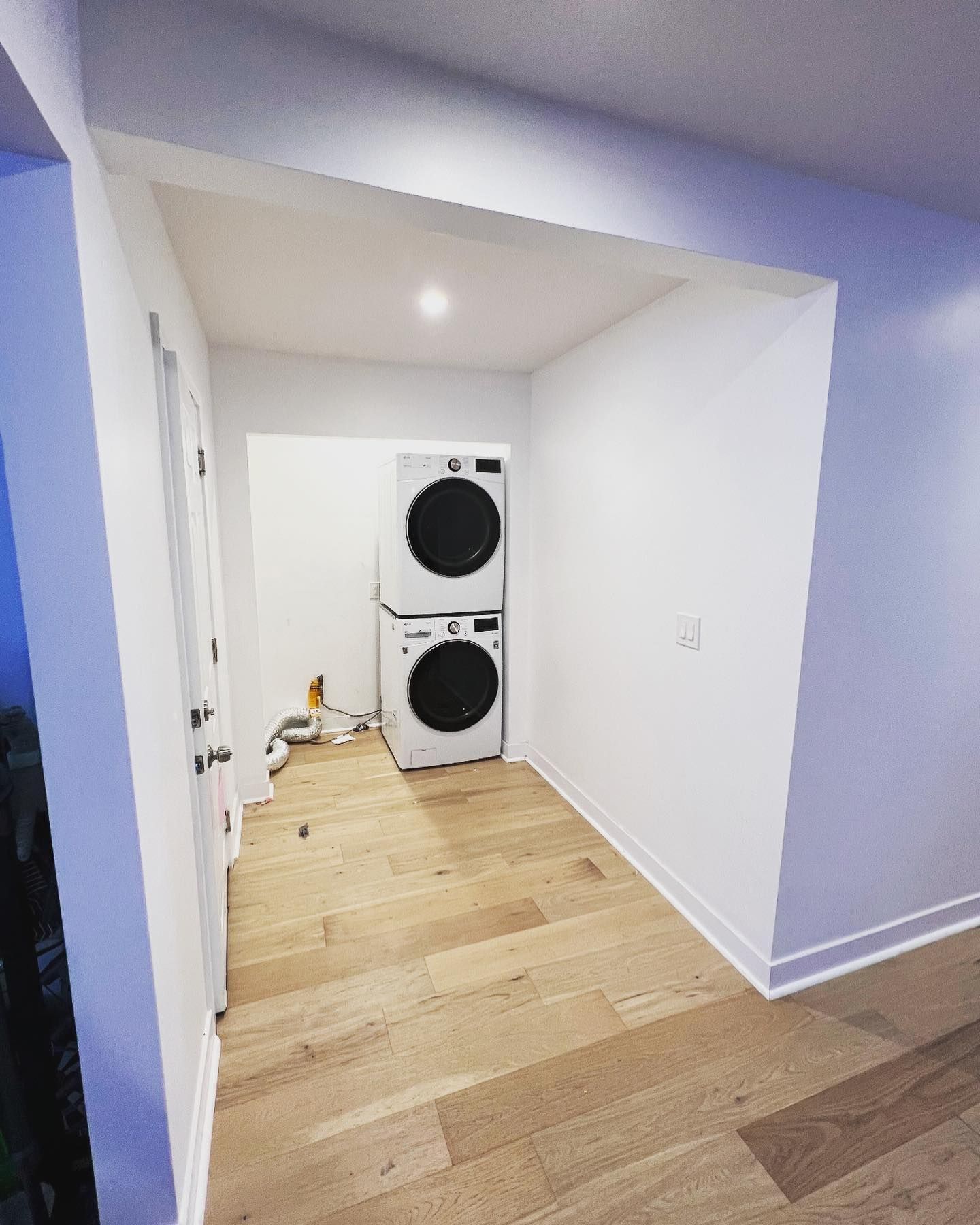 Laundry room with stacked white washer/dryer on wooden floor. White walls and doorway.