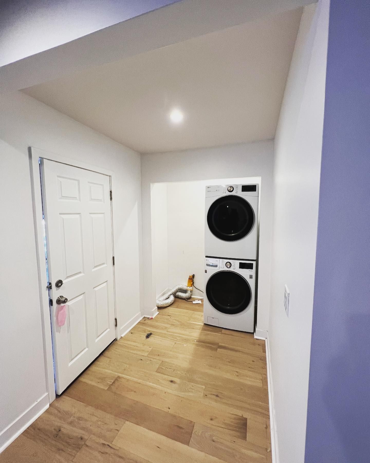 Laundry room with stacked white washer and dryer, a white door, and wood flooring.