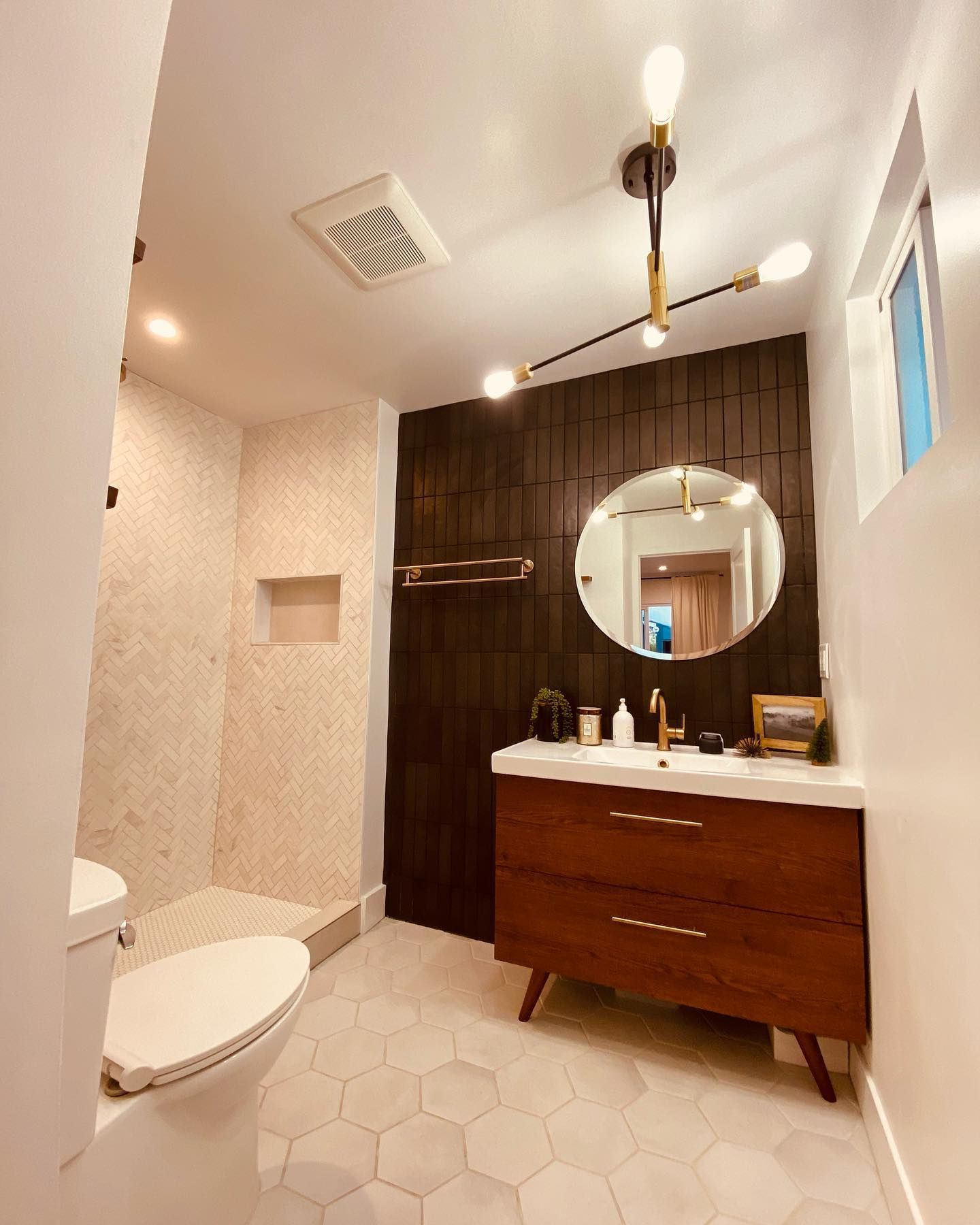 Modern bathroom with dark wood accent wall, round mirror, wood vanity, and hexagonal floor tiles.