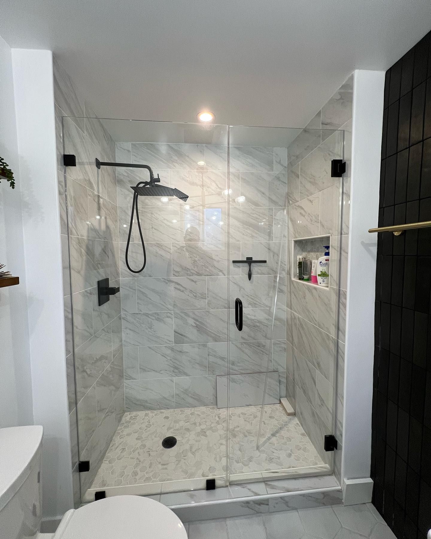 Glass shower with marble tile, black fixtures, and door.
