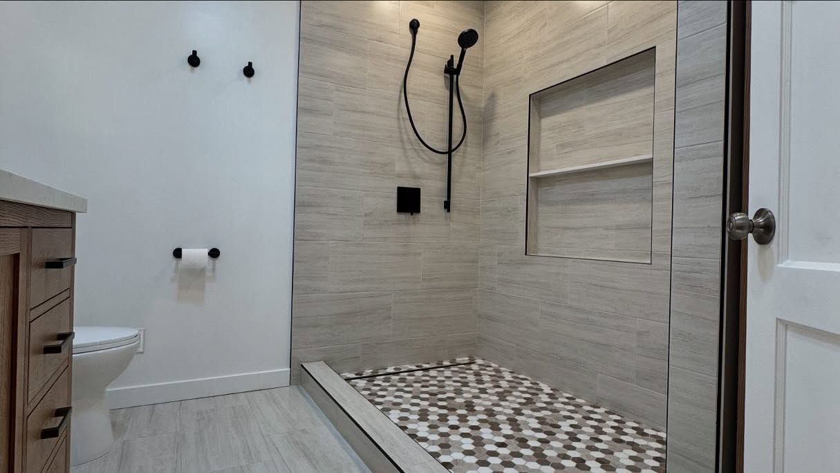 Bathroom with stone tile shower, pebble floor, and wood vanity.