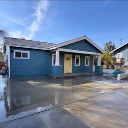 Blue house with yellow door, white pillars, and wet concrete driveway under a blue sky.