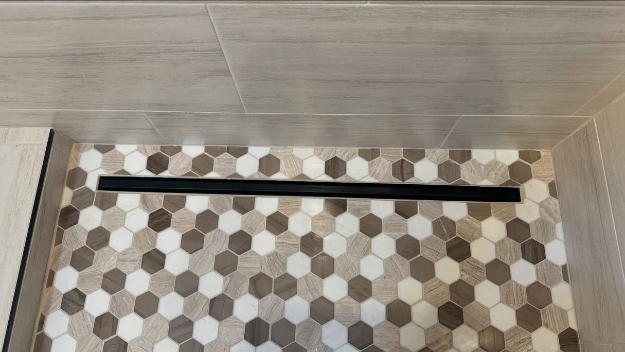Shower with dark rectangular drain set into hexagonal tile floor.