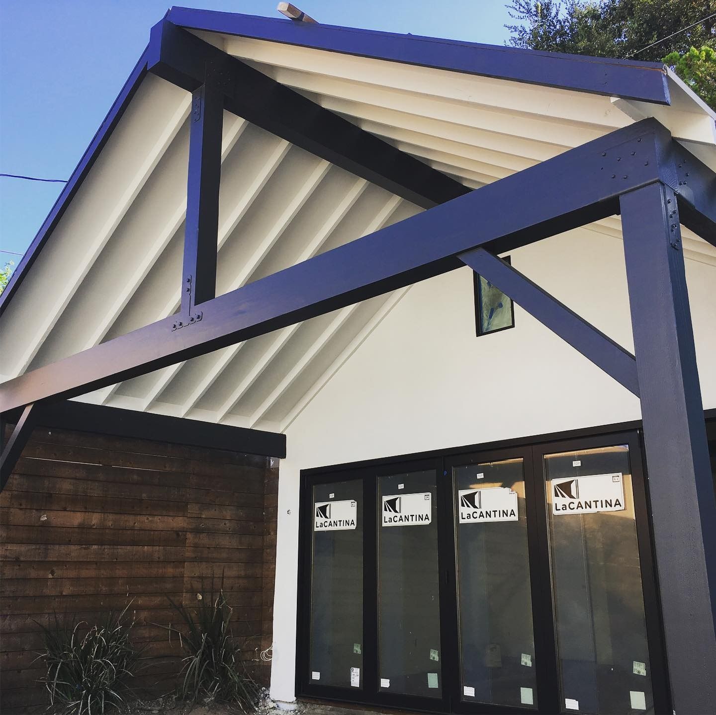 White building with black trim and large glass doors under a blue sky.