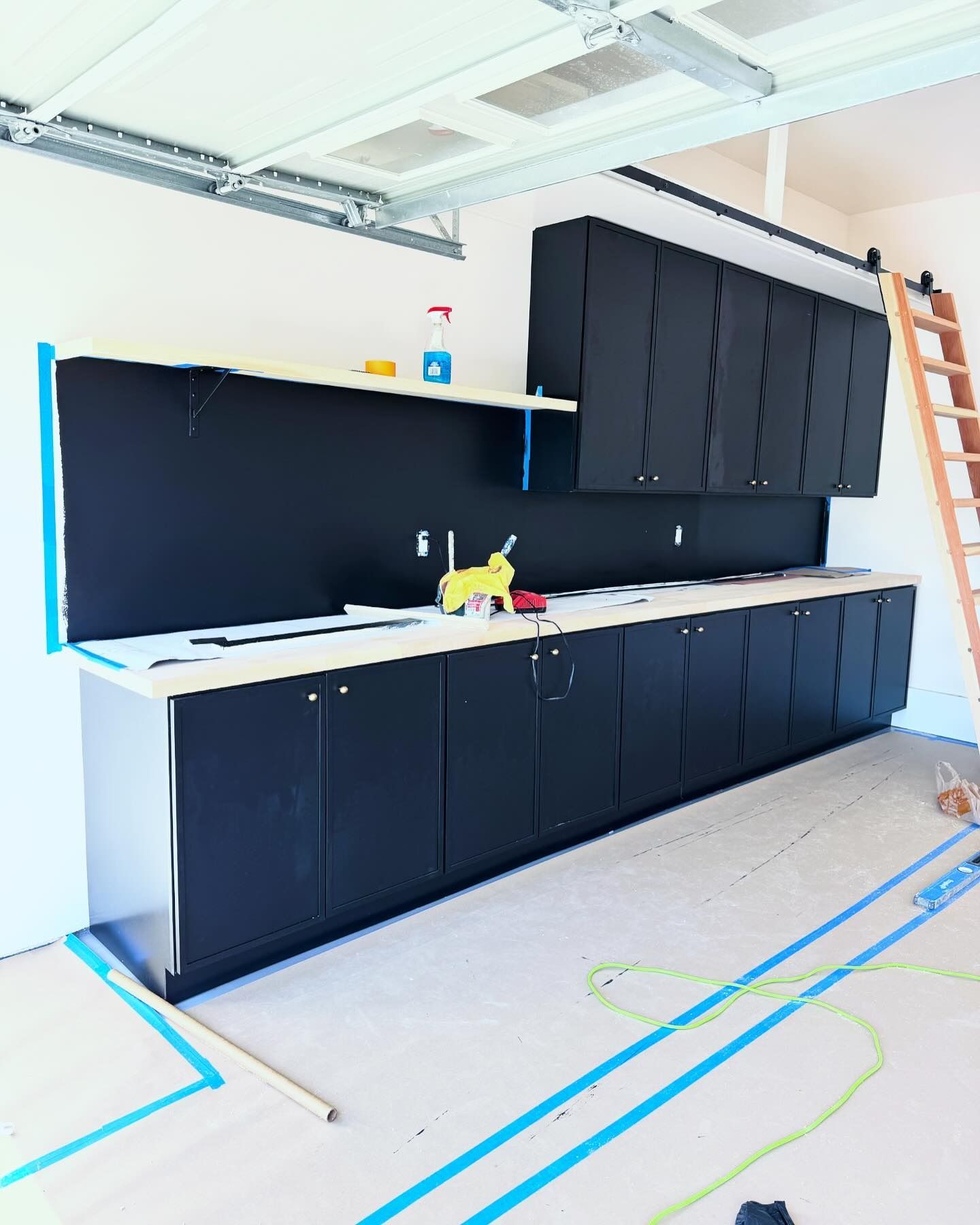Black cabinets and workbench installed in a garage, with a ladder on the right side.