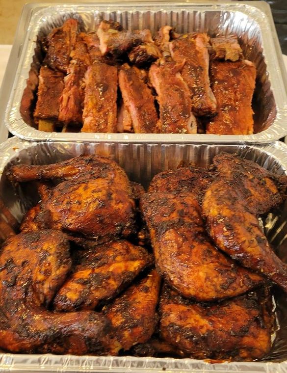 Two trays of meat , ribs and chicken , are sitting on a table.