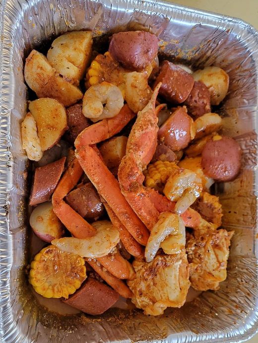 A foil container filled with crab legs , shrimp , corn , potatoes and sausage.