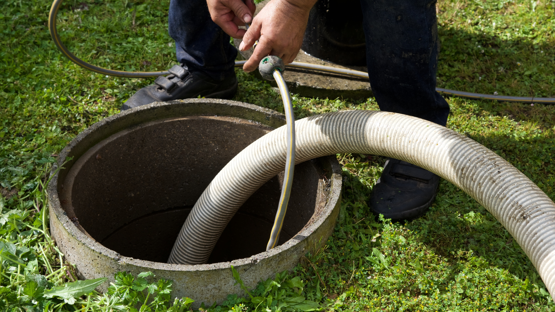 A man is pumping water into a septic tank with a hose.