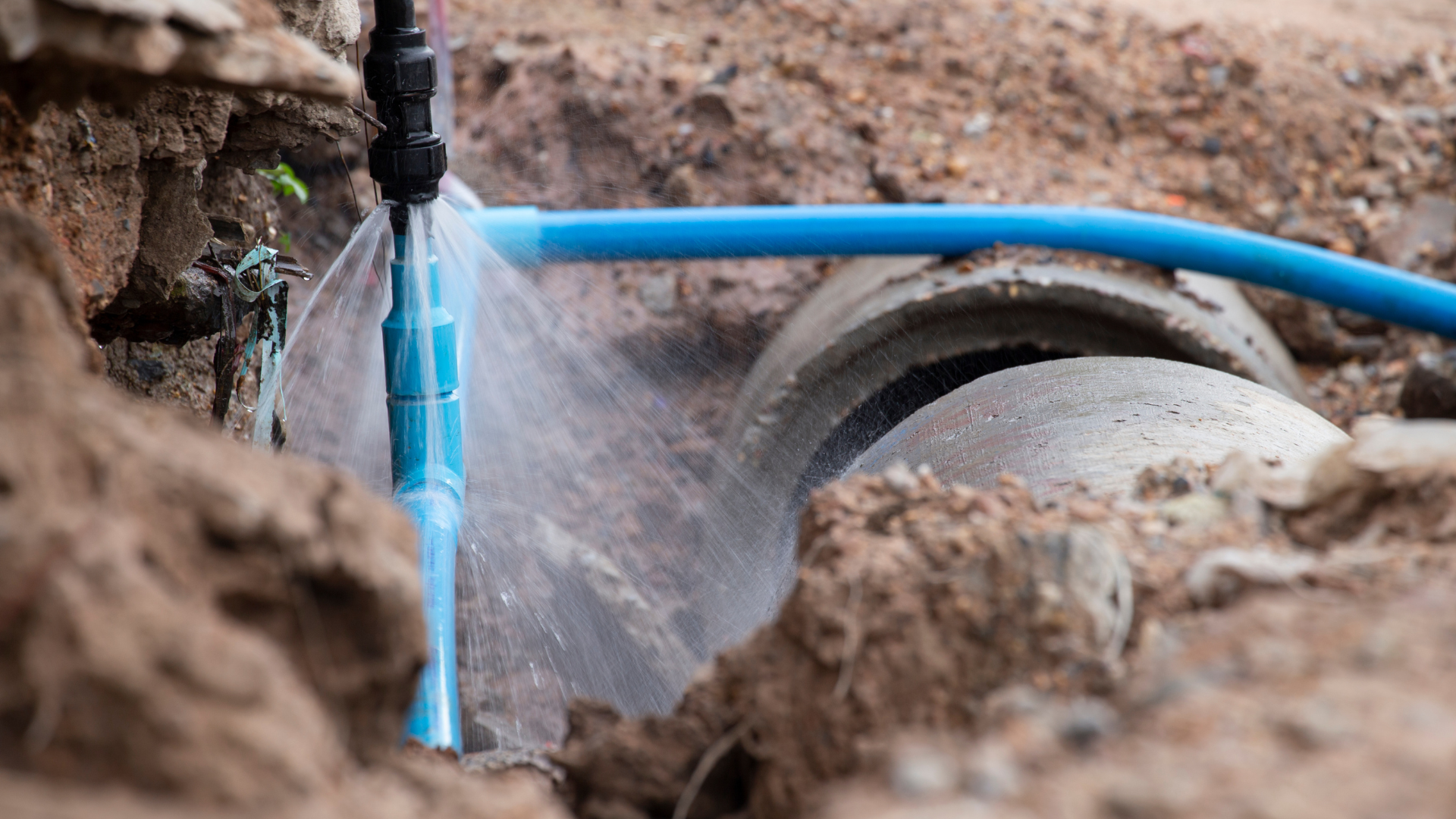 A hose is spraying water on a pipe in the dirt.