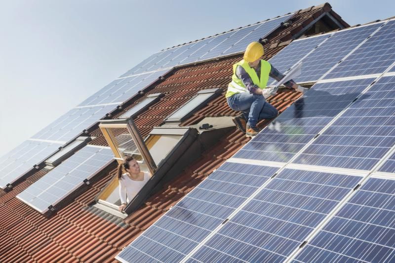 Un uomo e una donna stanno installando dei pannelli solari sul tetto di una casa.