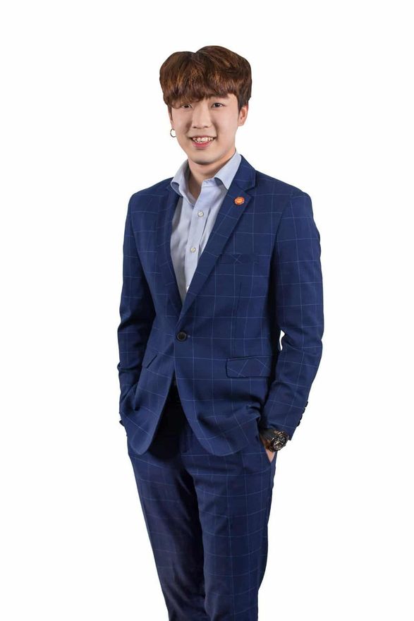 Young man smiles, wearing a blue suit, open-collar light blue shirt, and small earring.
