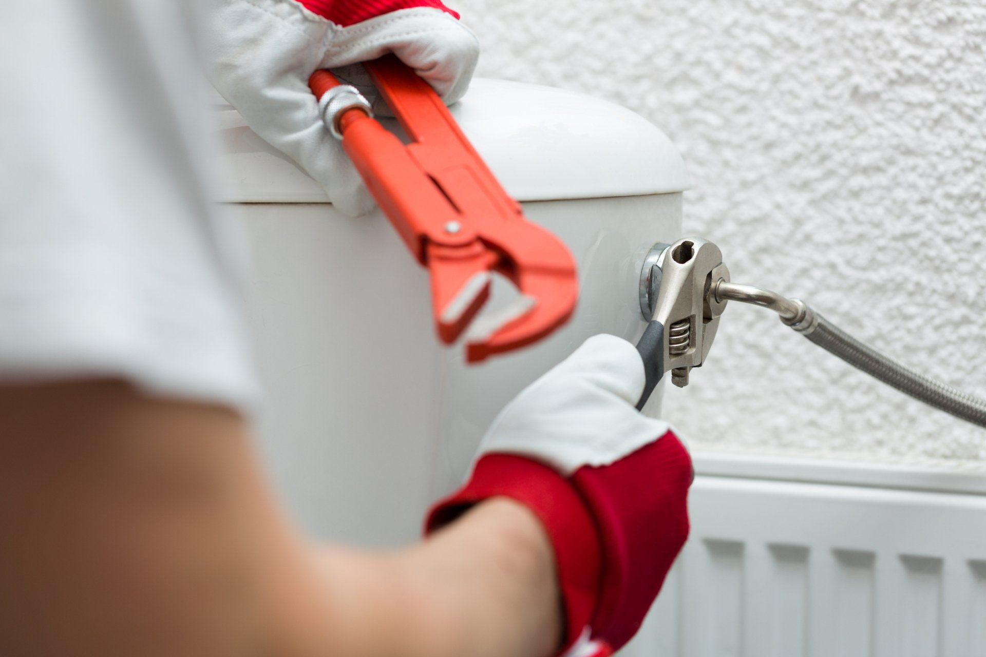 A person is fixing a toilet with a wrench.