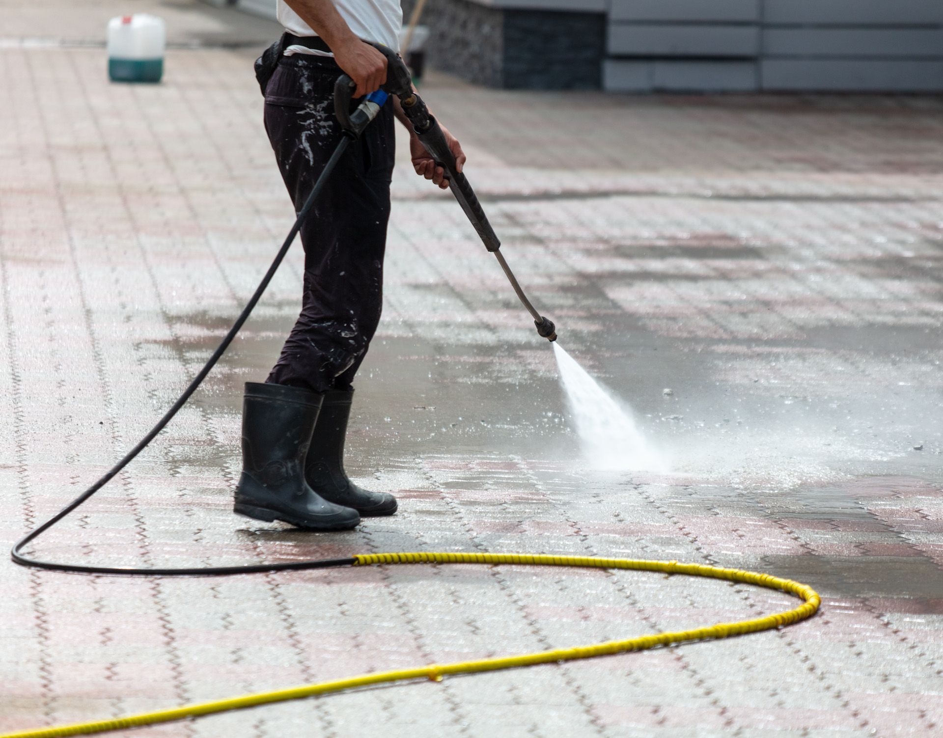 A person is using a high pressure washer to clean a brick sidewalk.