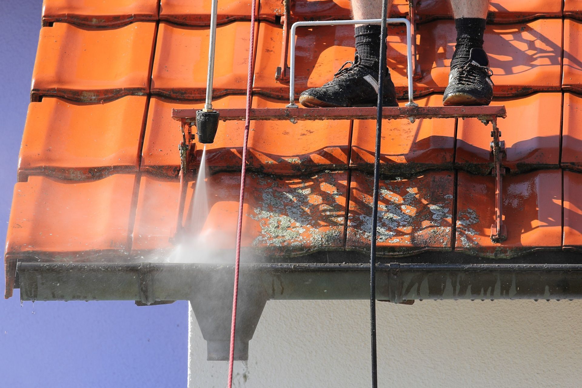 A man is standing on a ladder cleaning a roof with a high pressure washer.
