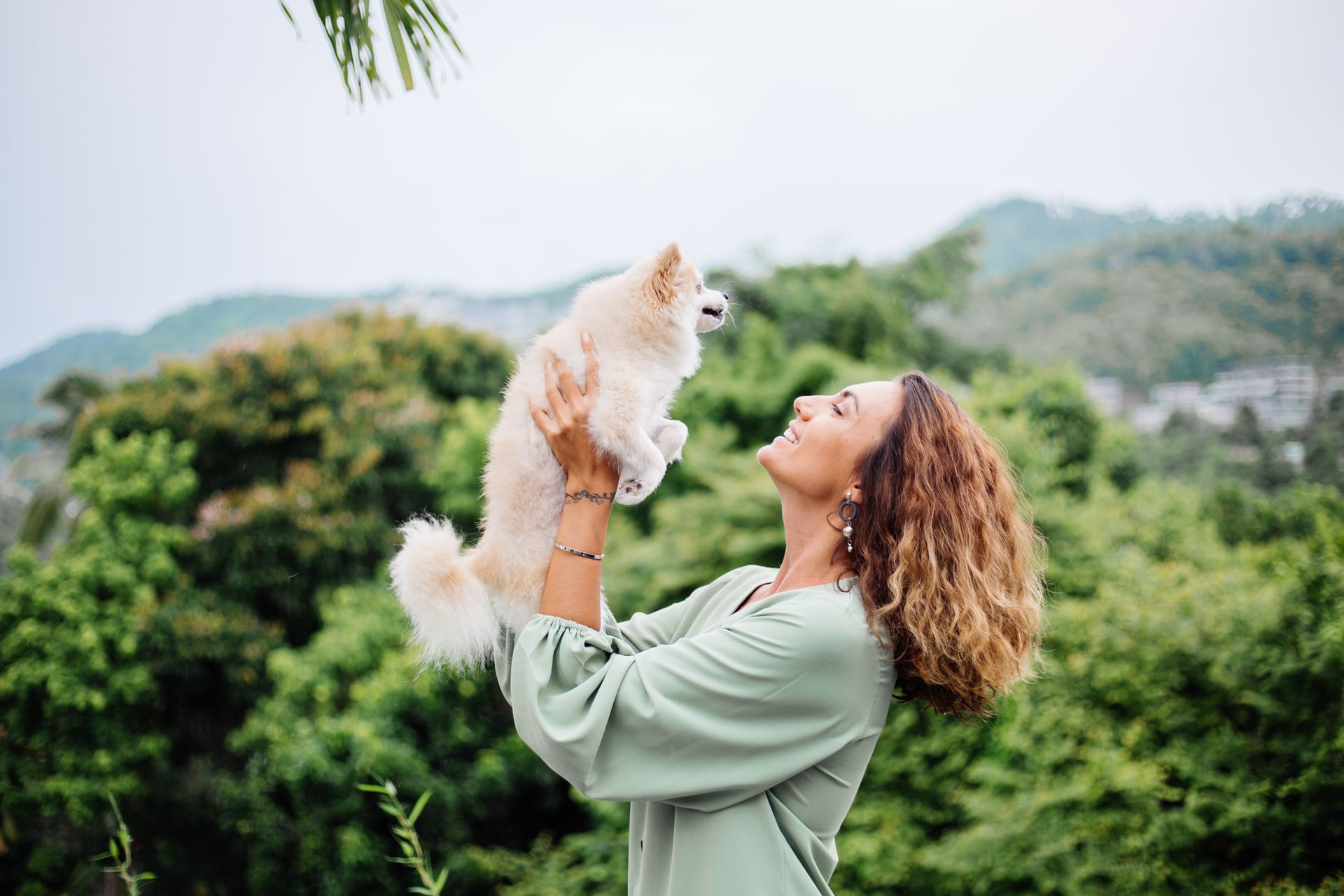 A woman is carrying her dog in her arms and playing in an outdoor setting.