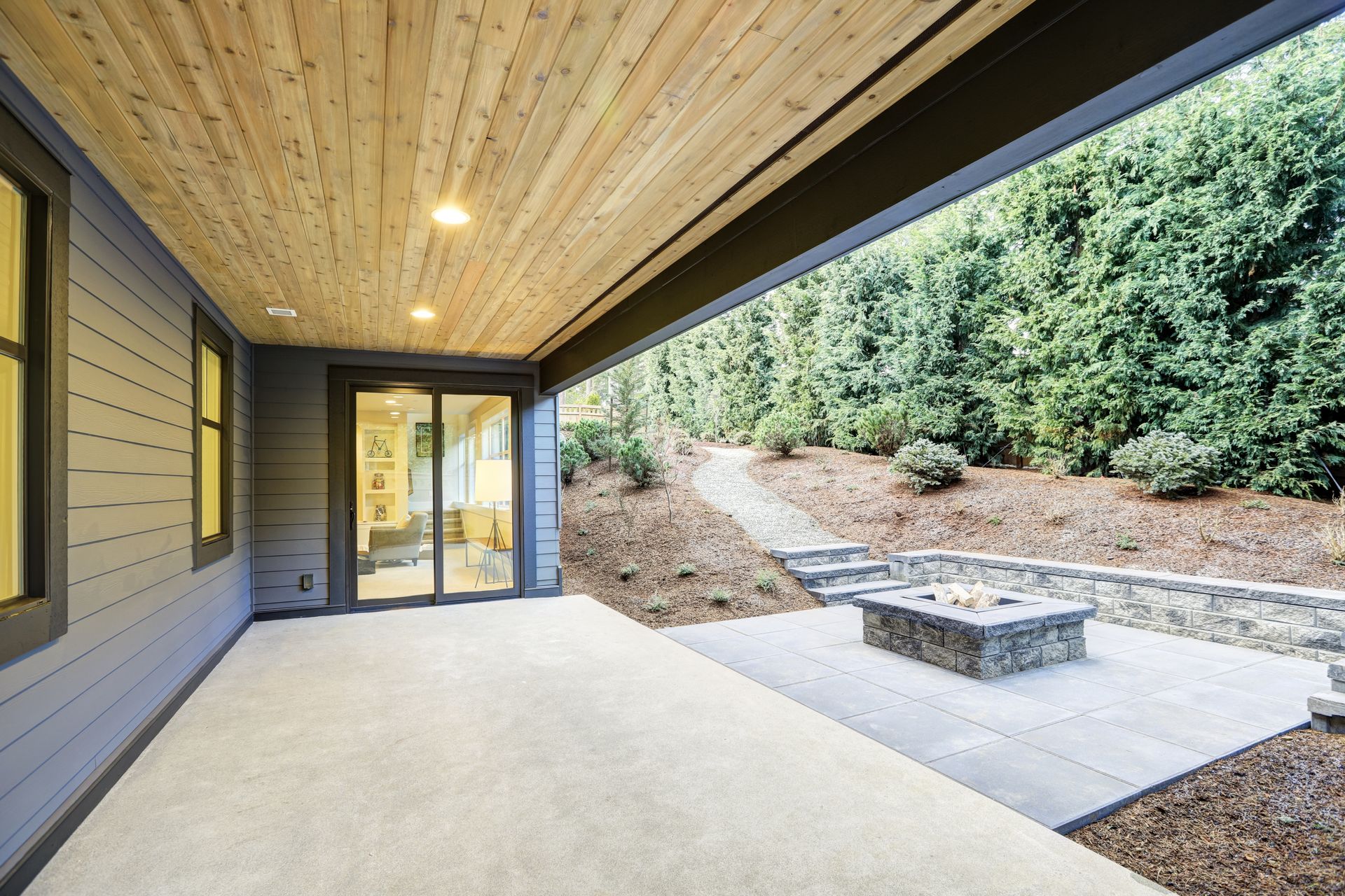 Covered patio with light-colored flooring, wood ceiling, and sliding glass doors.  A stone fire pit is in the backyard.