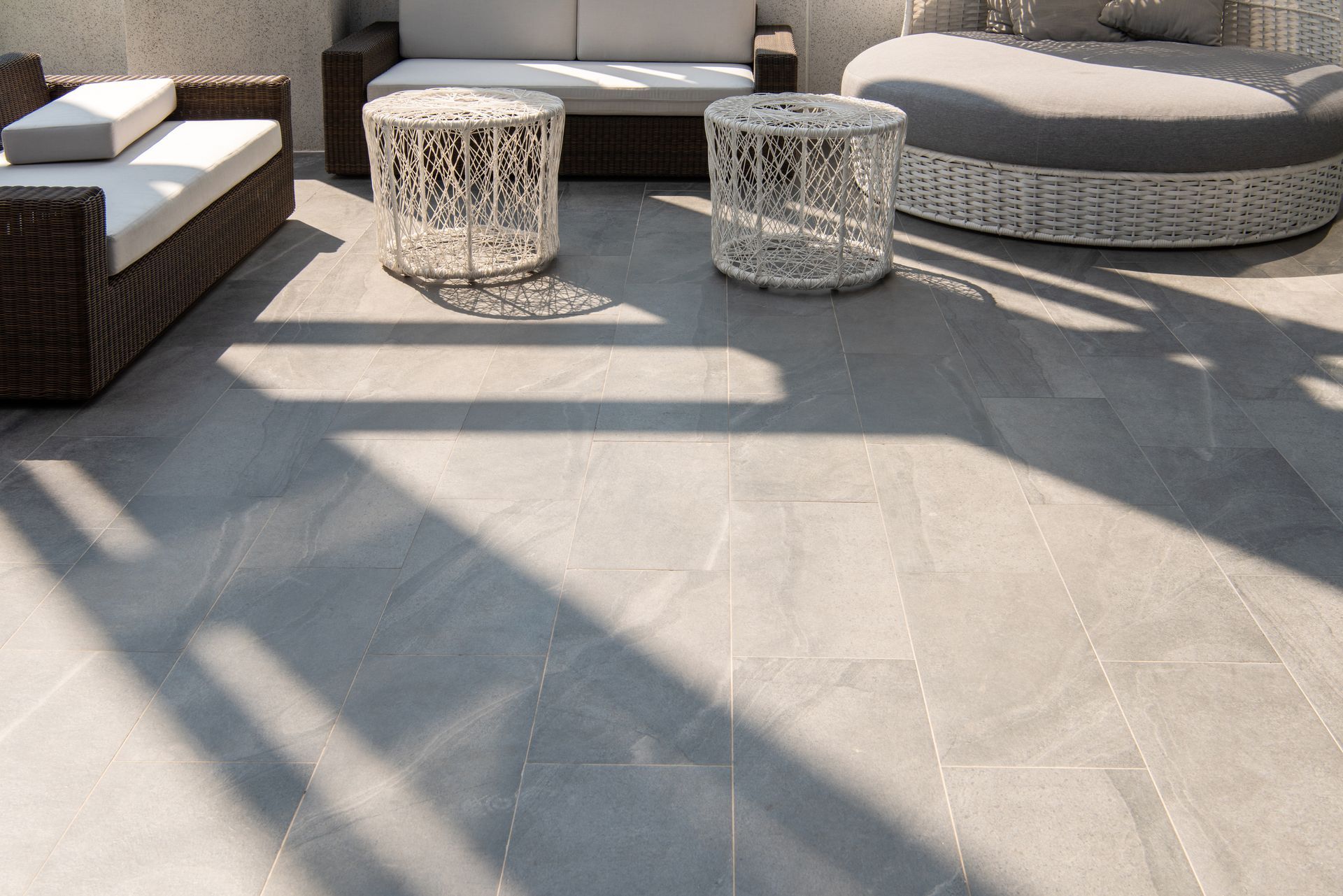 Patio with gray stone flooring, wicker furniture, and sunlight shadows.