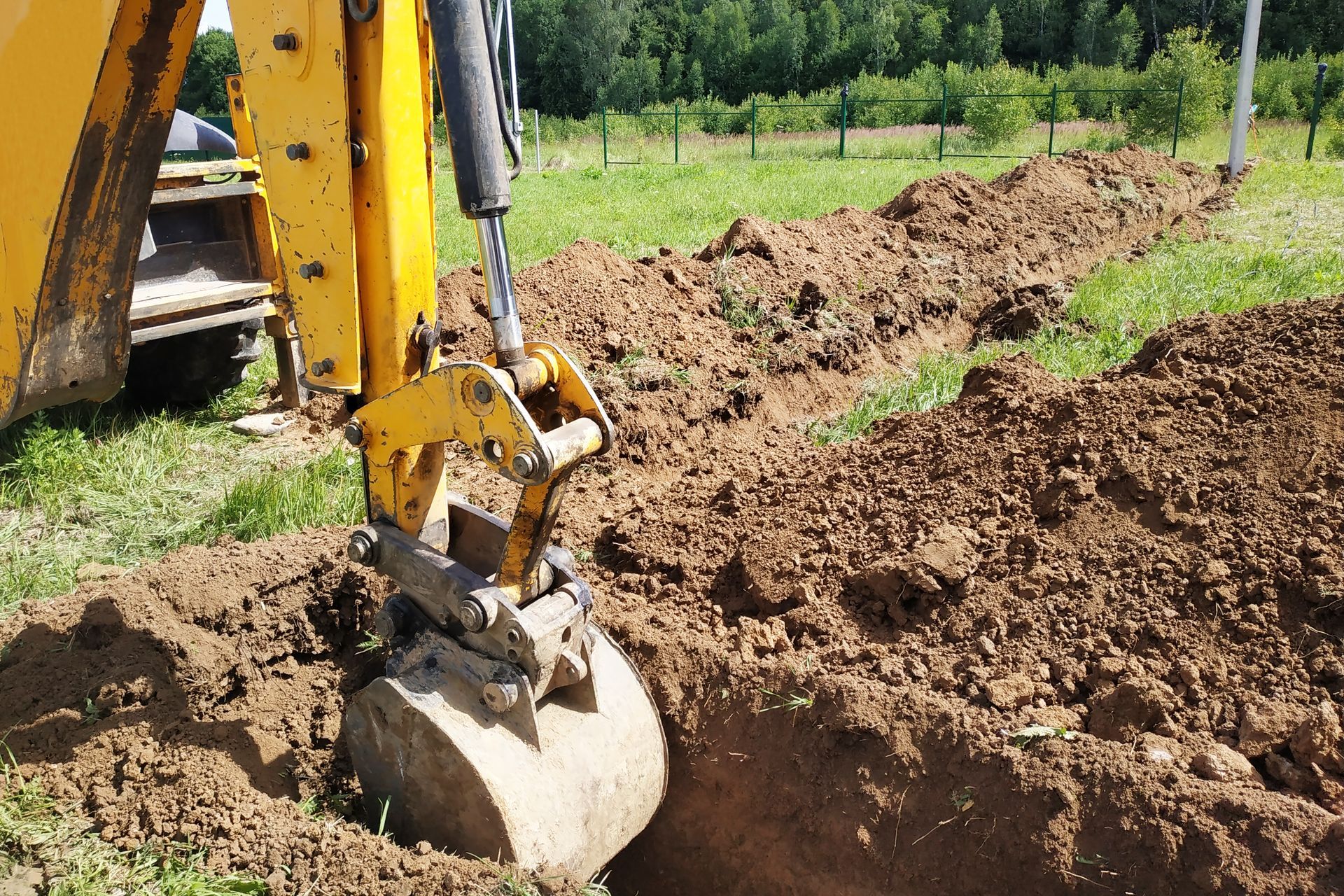 Yellow excavator digging a trench in a grassy field.