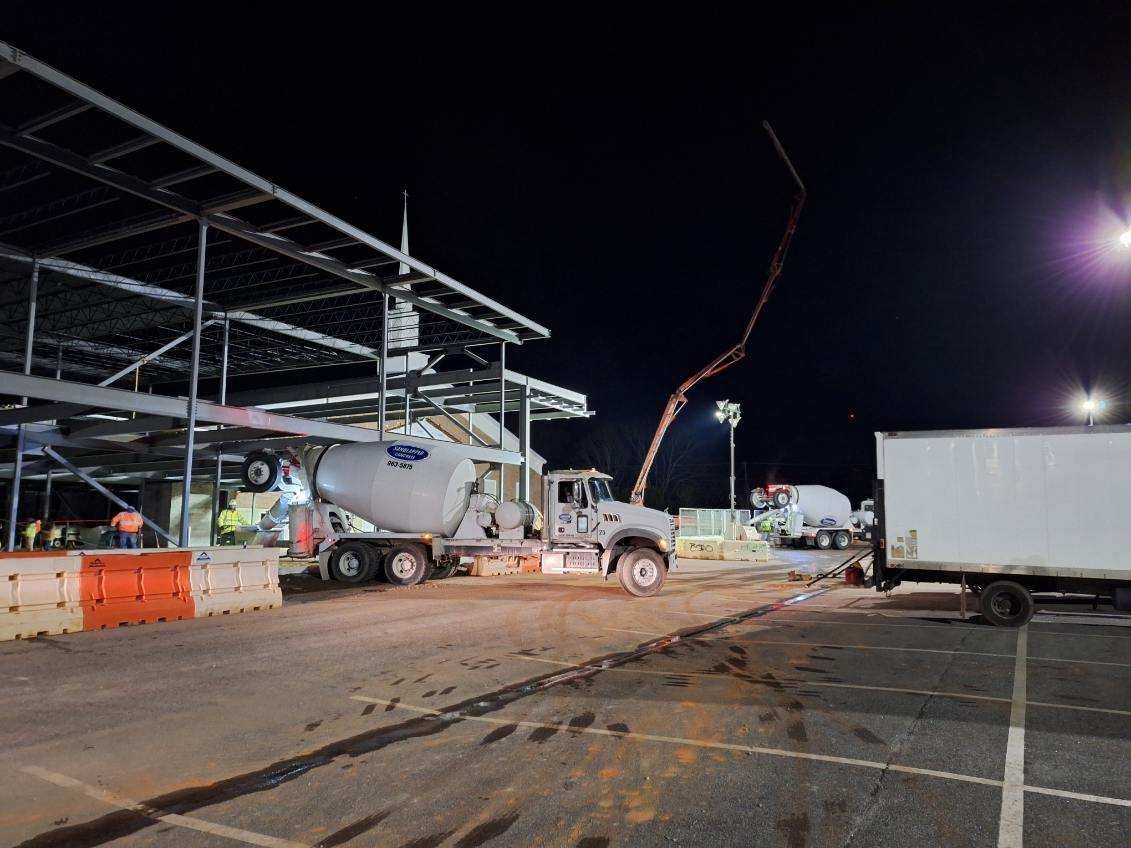 A concrete mixer truck is driving down a construction site at night.