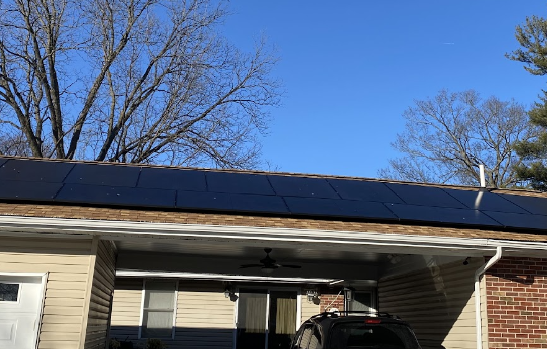 A car is parked in front of a house with solar panels on the roof.