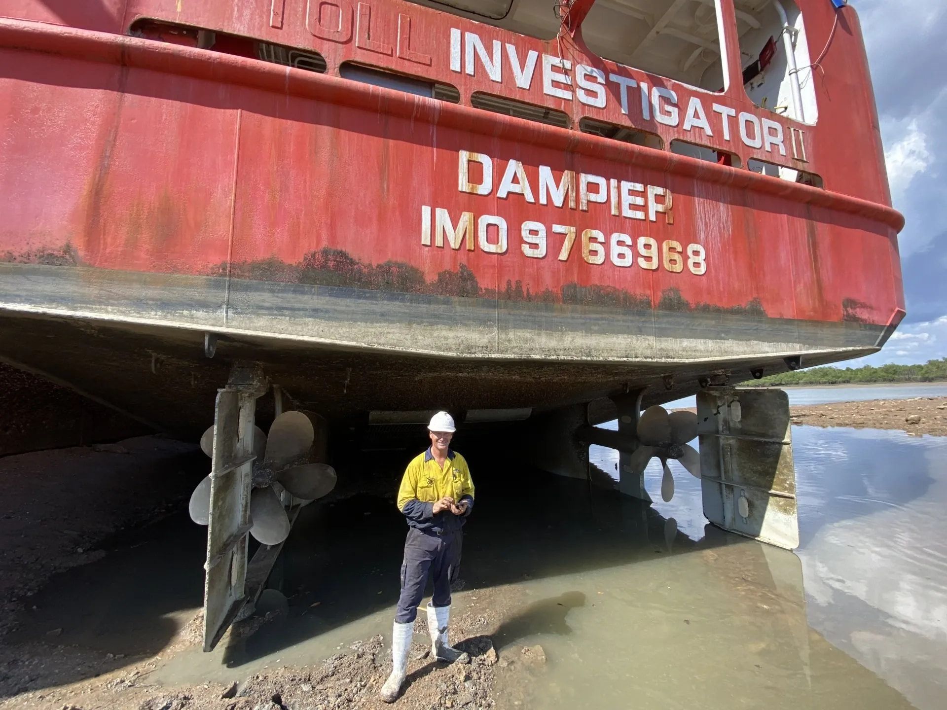 A man in hi-vis is standing underneath a large ship — ElectroMech Machine in Woolner, NT
