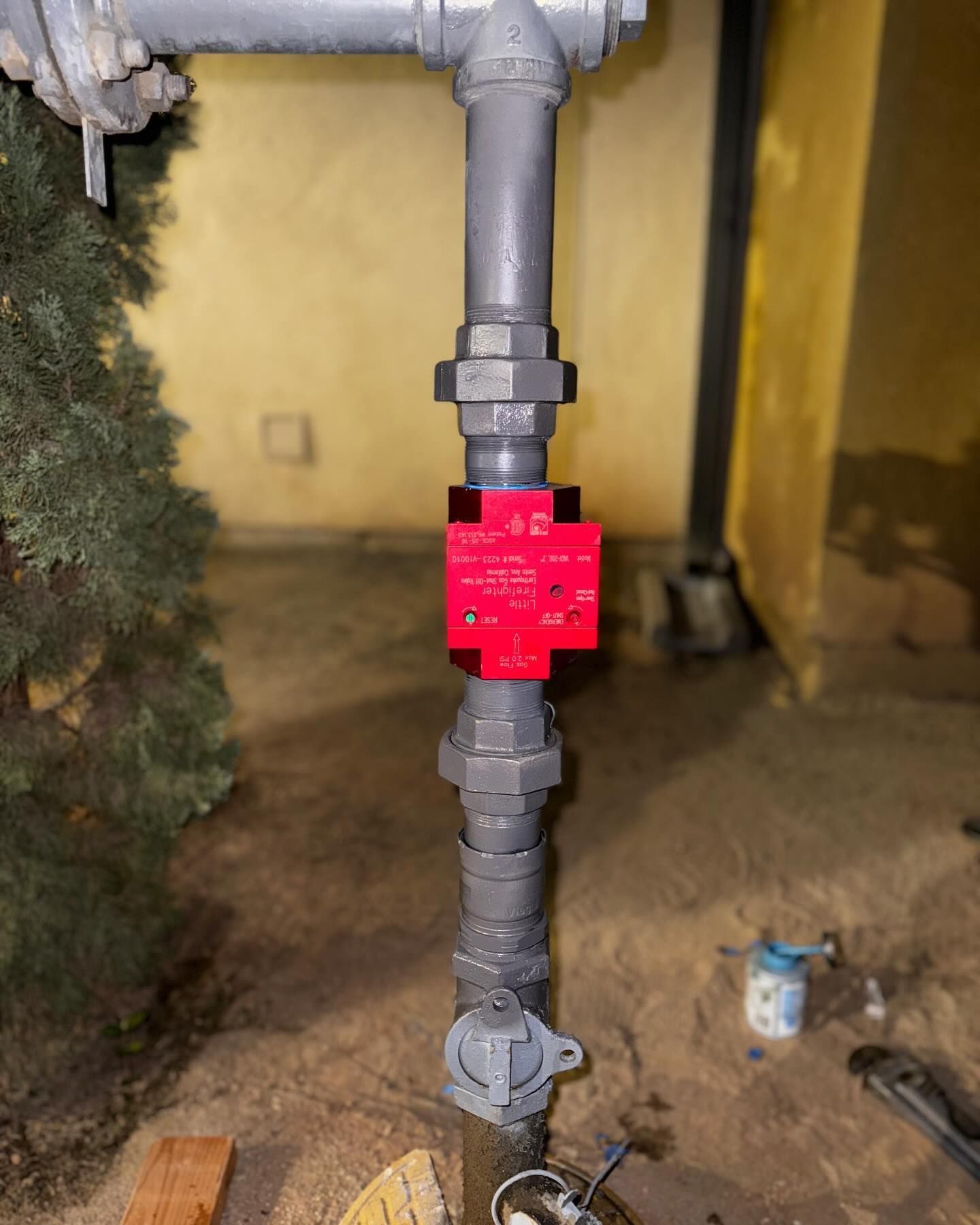Vertical grey gas pipe with a red safety valve, outdoors.