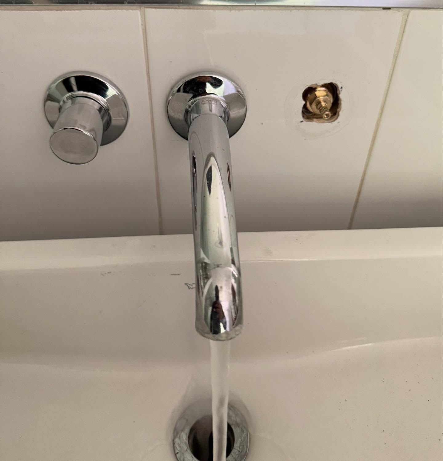 A faucet with water flowing into a white sink. A missing fixture is visible.