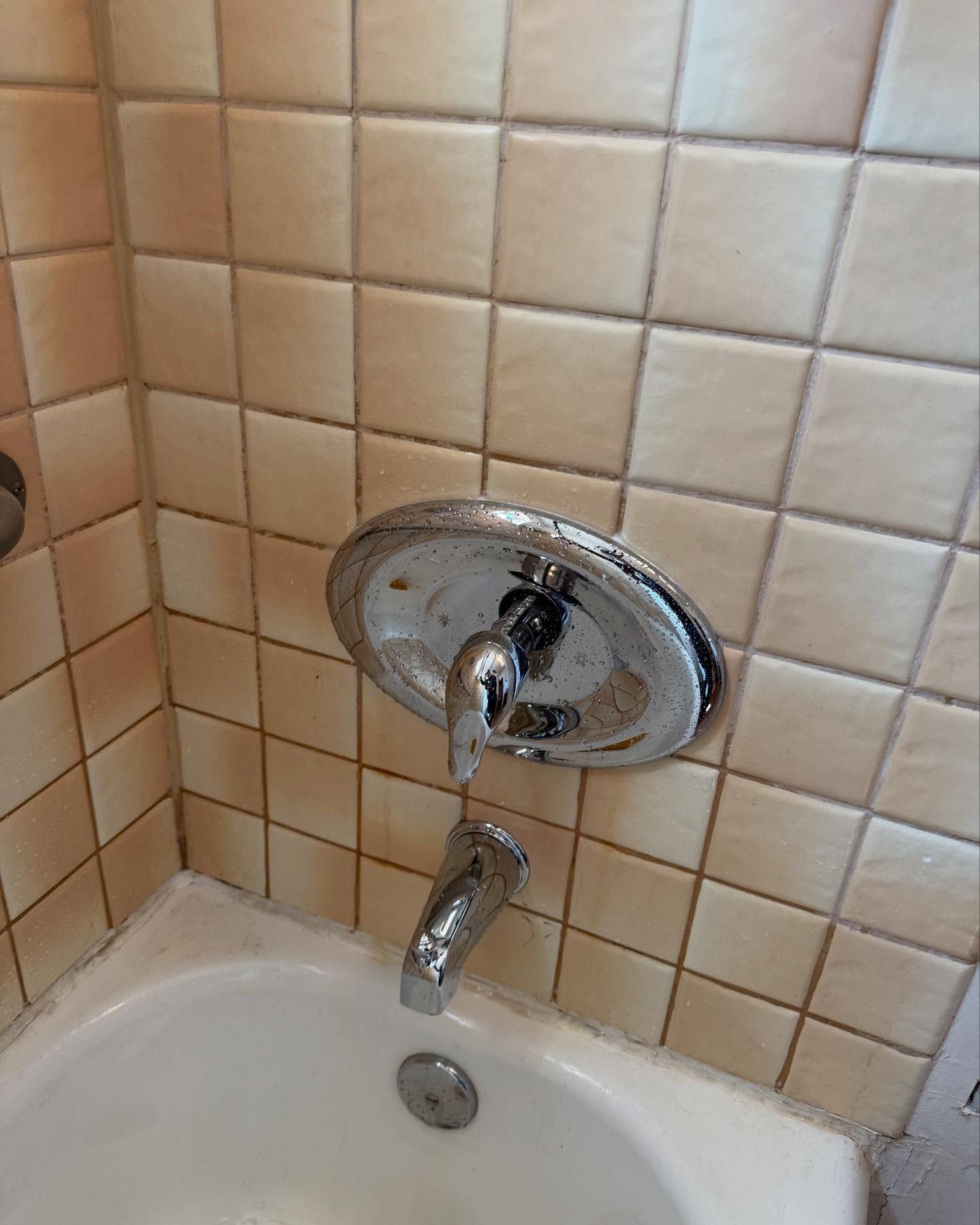 Chrome shower faucet on beige-tiled wall above a white bathtub.