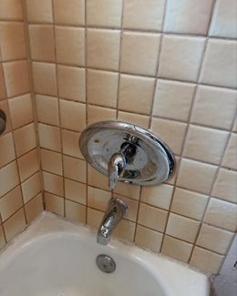 Chrome shower faucet on beige-tiled wall above a white bathtub.