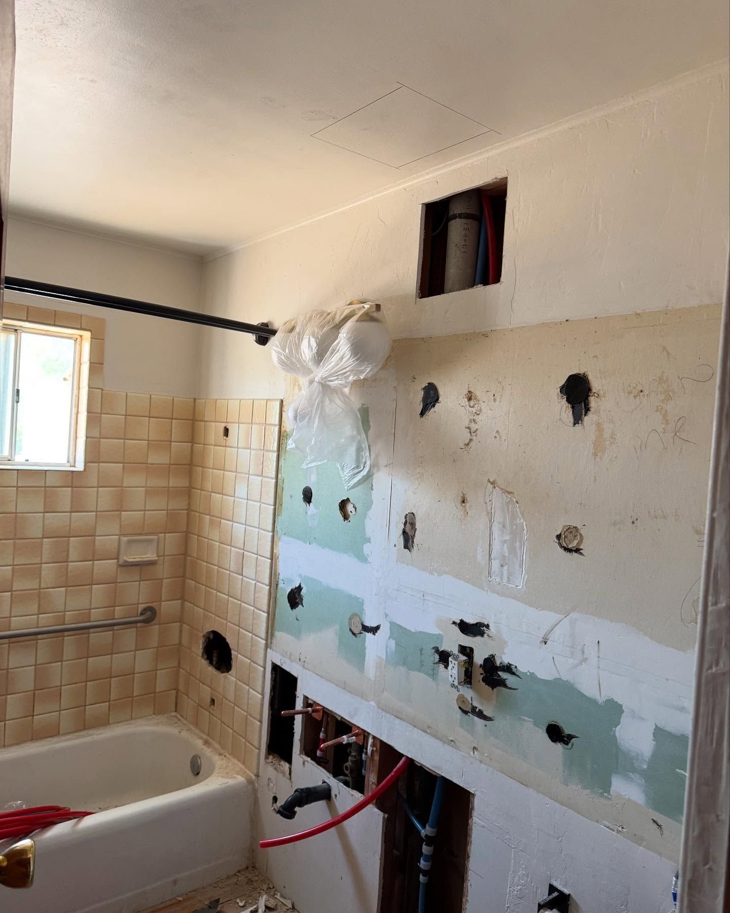 Bathroom under renovation; exposed wall studs, plumbing, and demolition debris visible near bathtub and shower rod.
