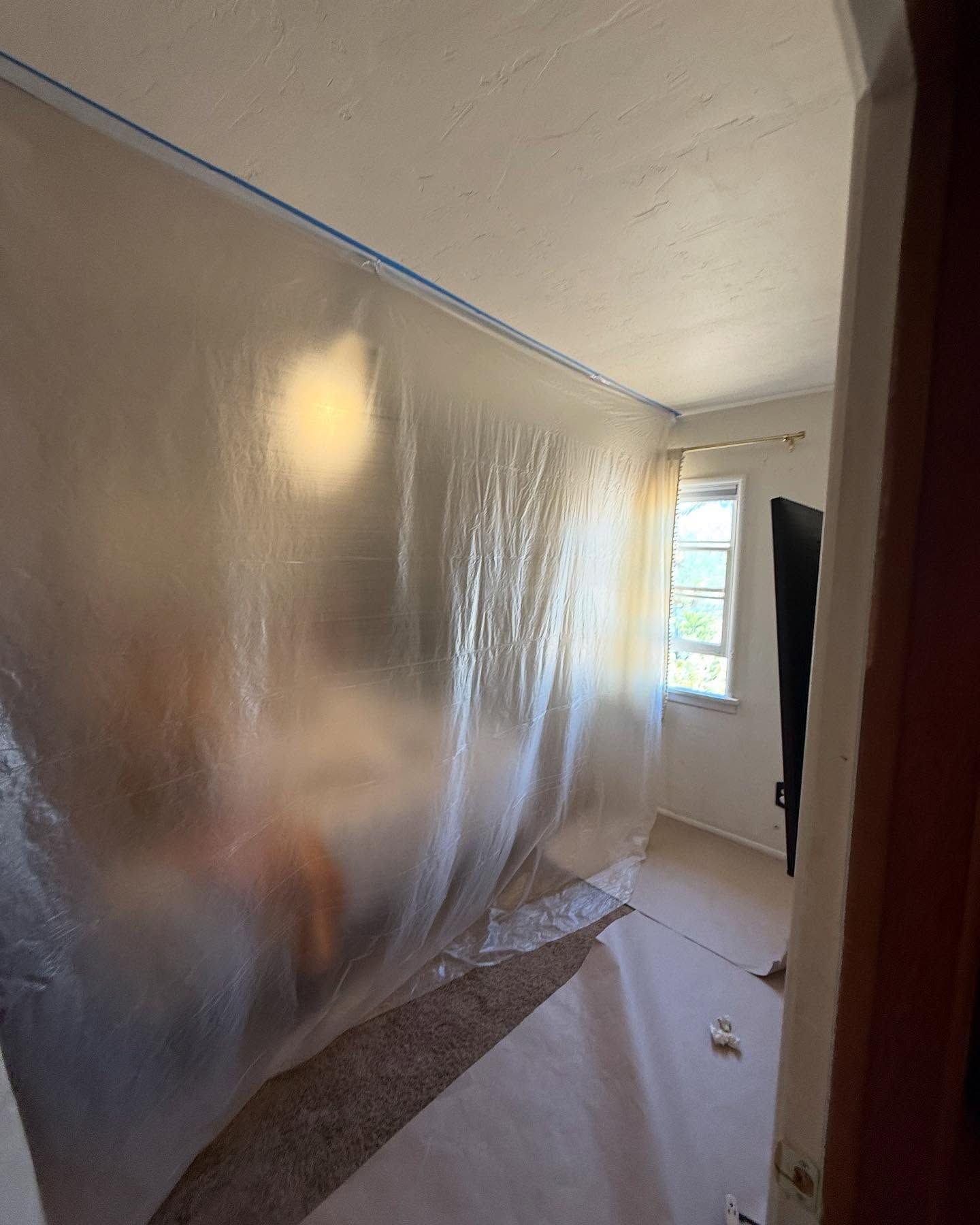 A room with plastic sheeting installed, likely for renovation. A window is visible.