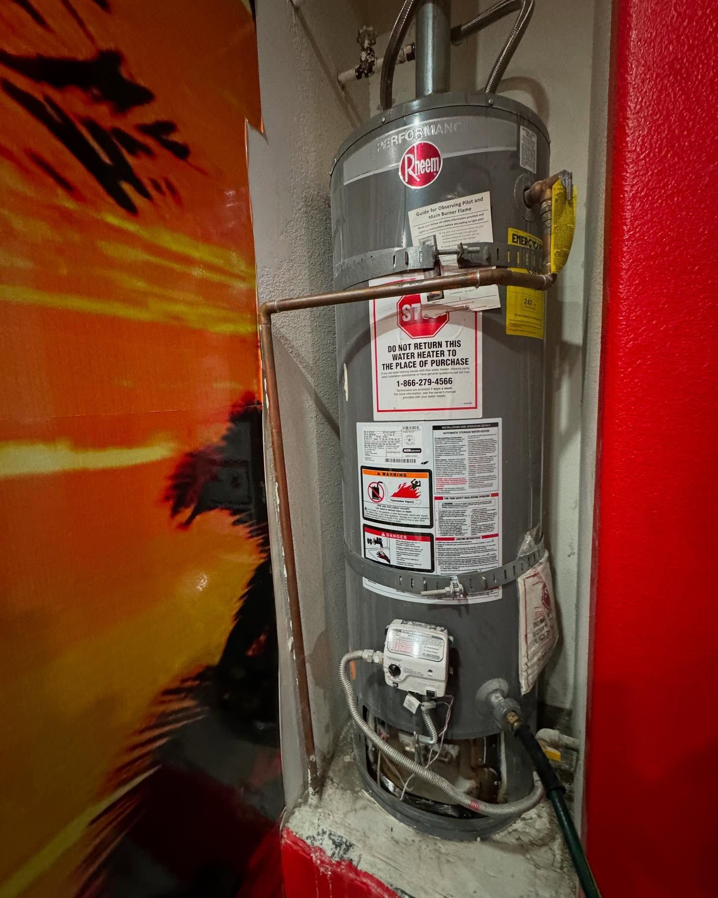 Water heater in a small enclosure, with copper pipes and safety labels.