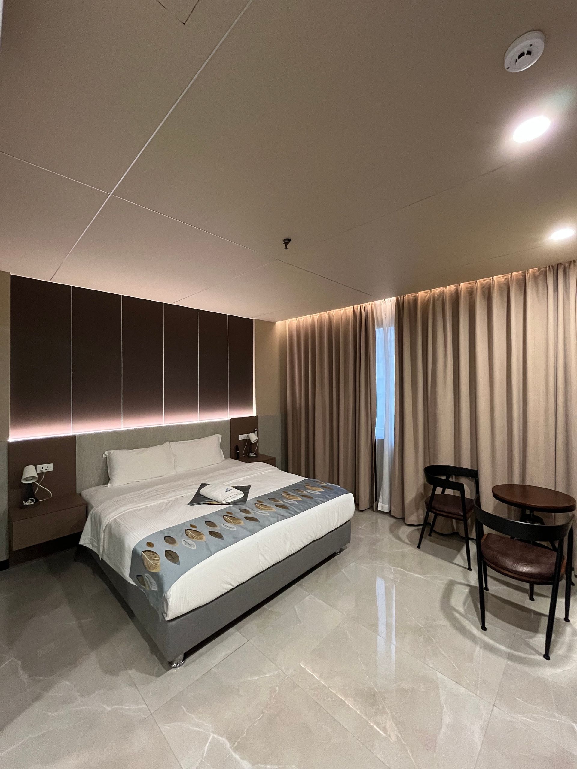 Modern hotel room with a bed, chairs, and window with curtains.