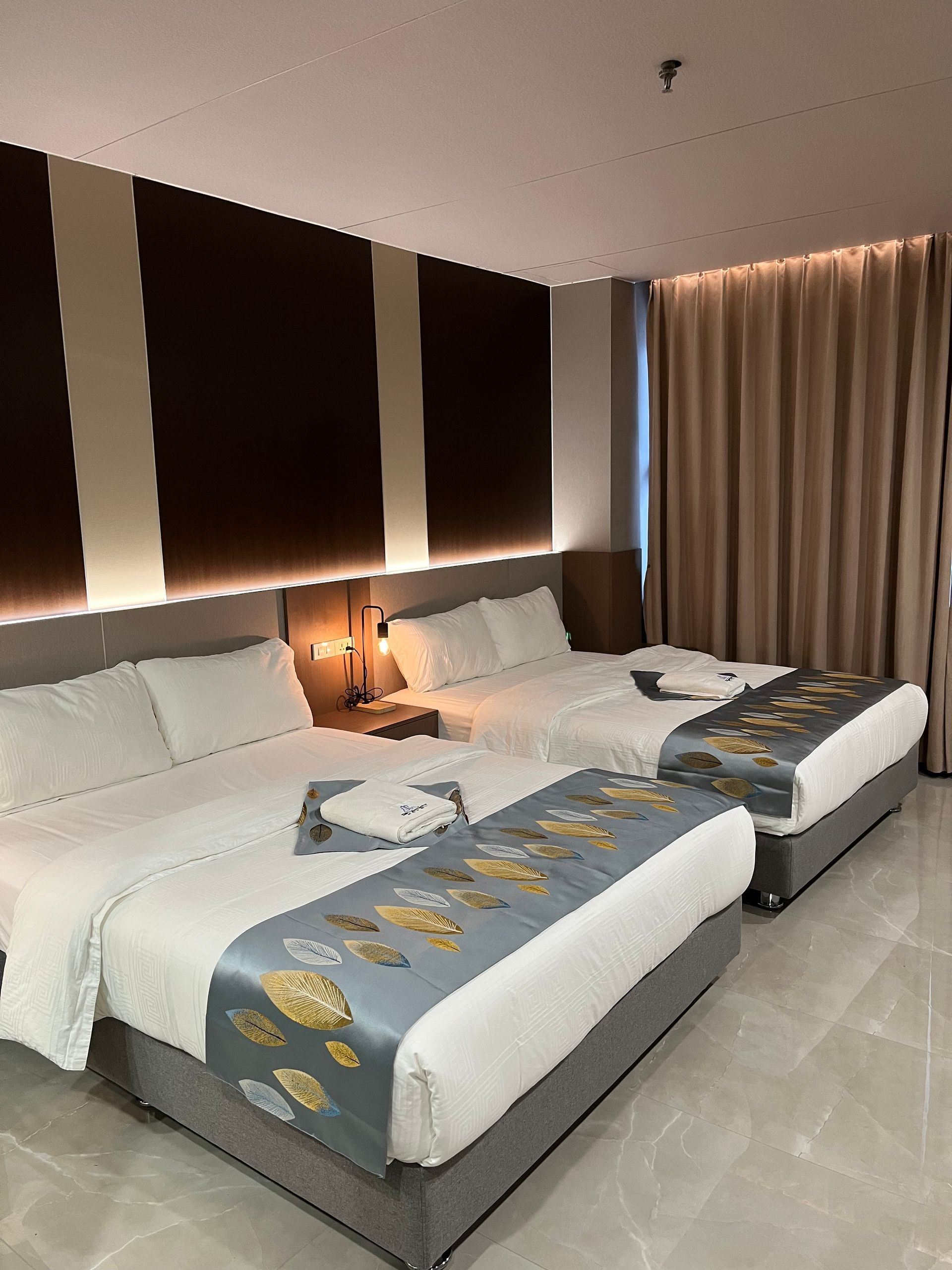 Hotel room with three beds, white linens, brown wall accents, and tan curtains.