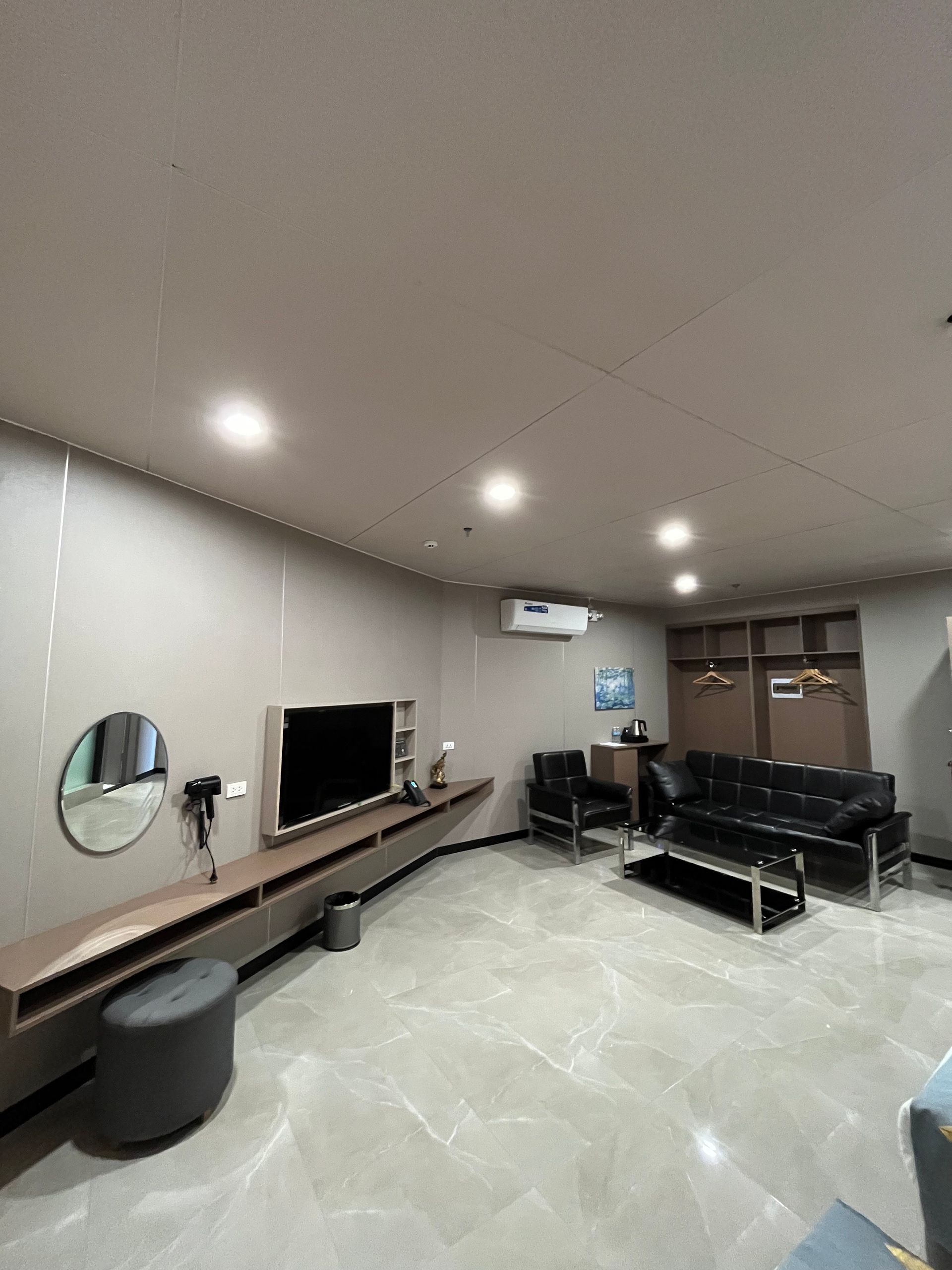 Modern living room with TV, black sofa, and gray walls, tiled floor.