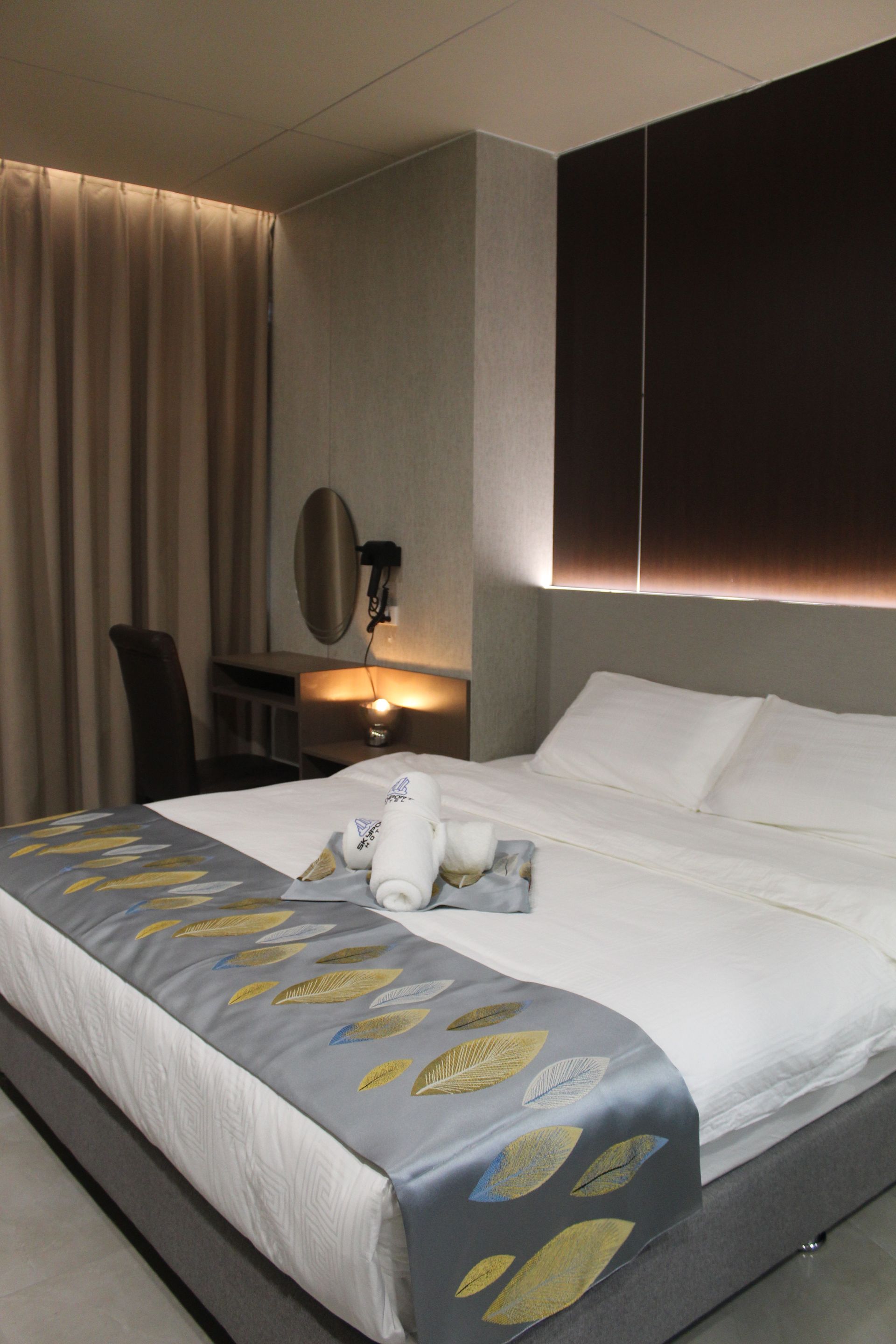 Hotel bedroom with a bed, desk, and window with brown blinds.
