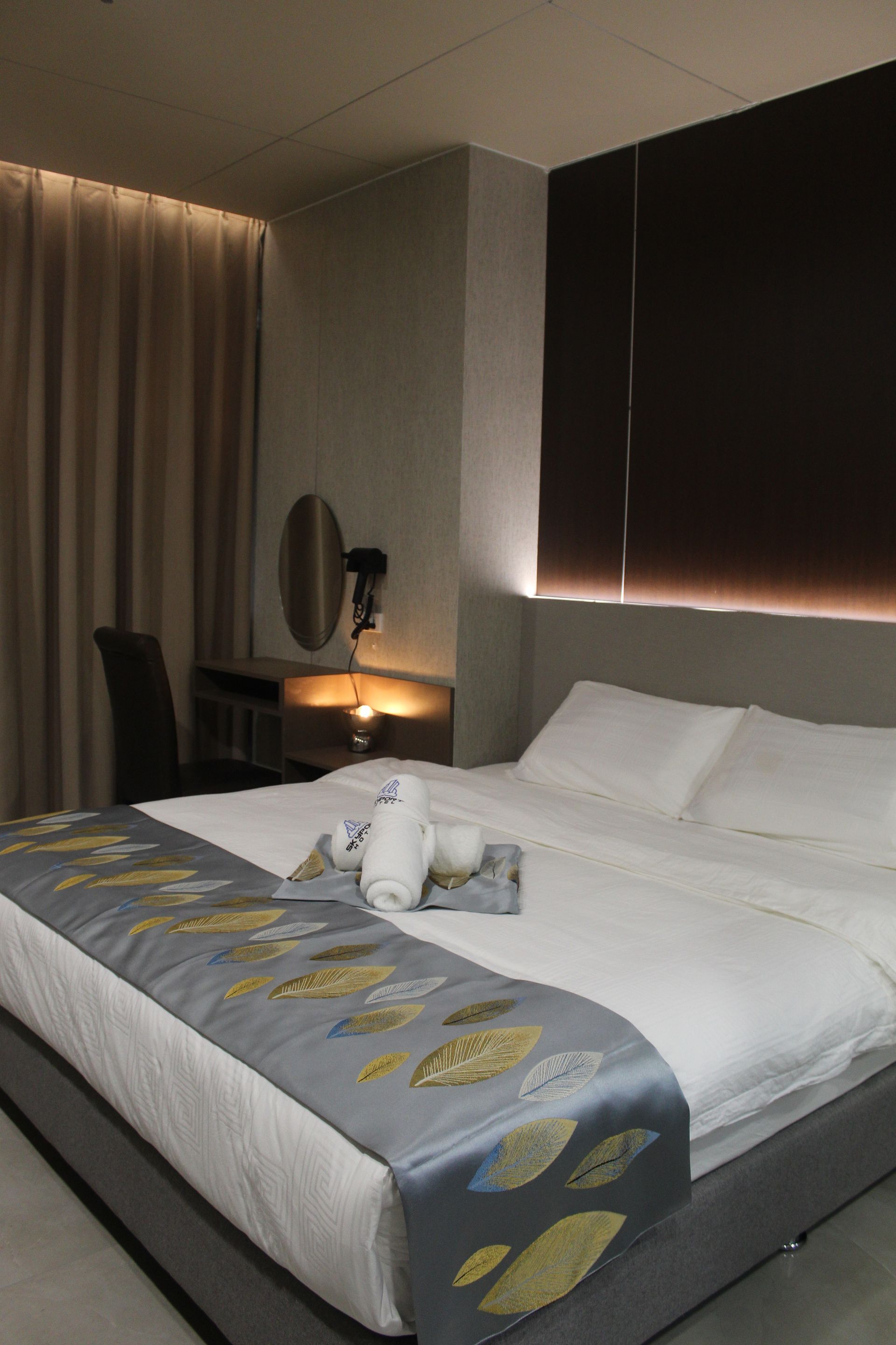 Hotel room with a bed, desk, and window. Bed has white linens and decorative runner.