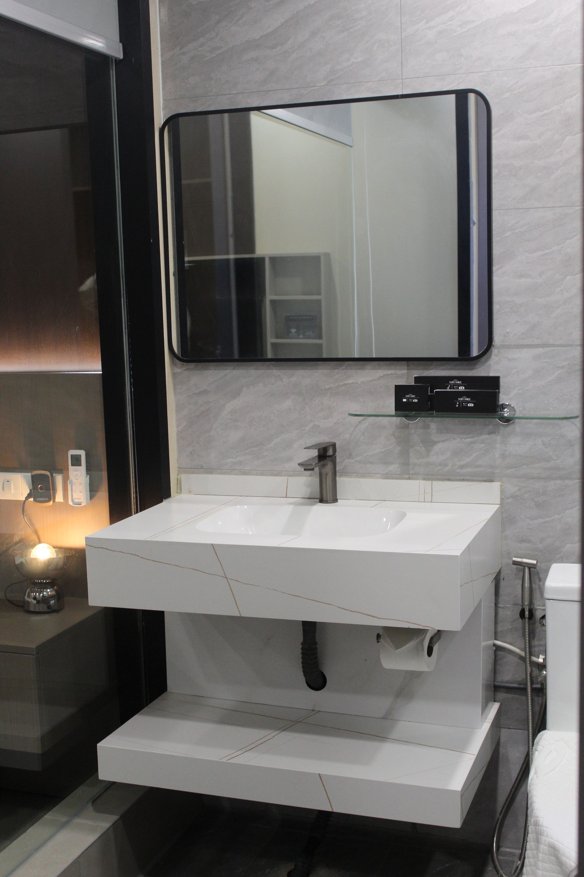 Modern bathroom with a white floating sink, a black-framed mirror, and gray tiled walls.