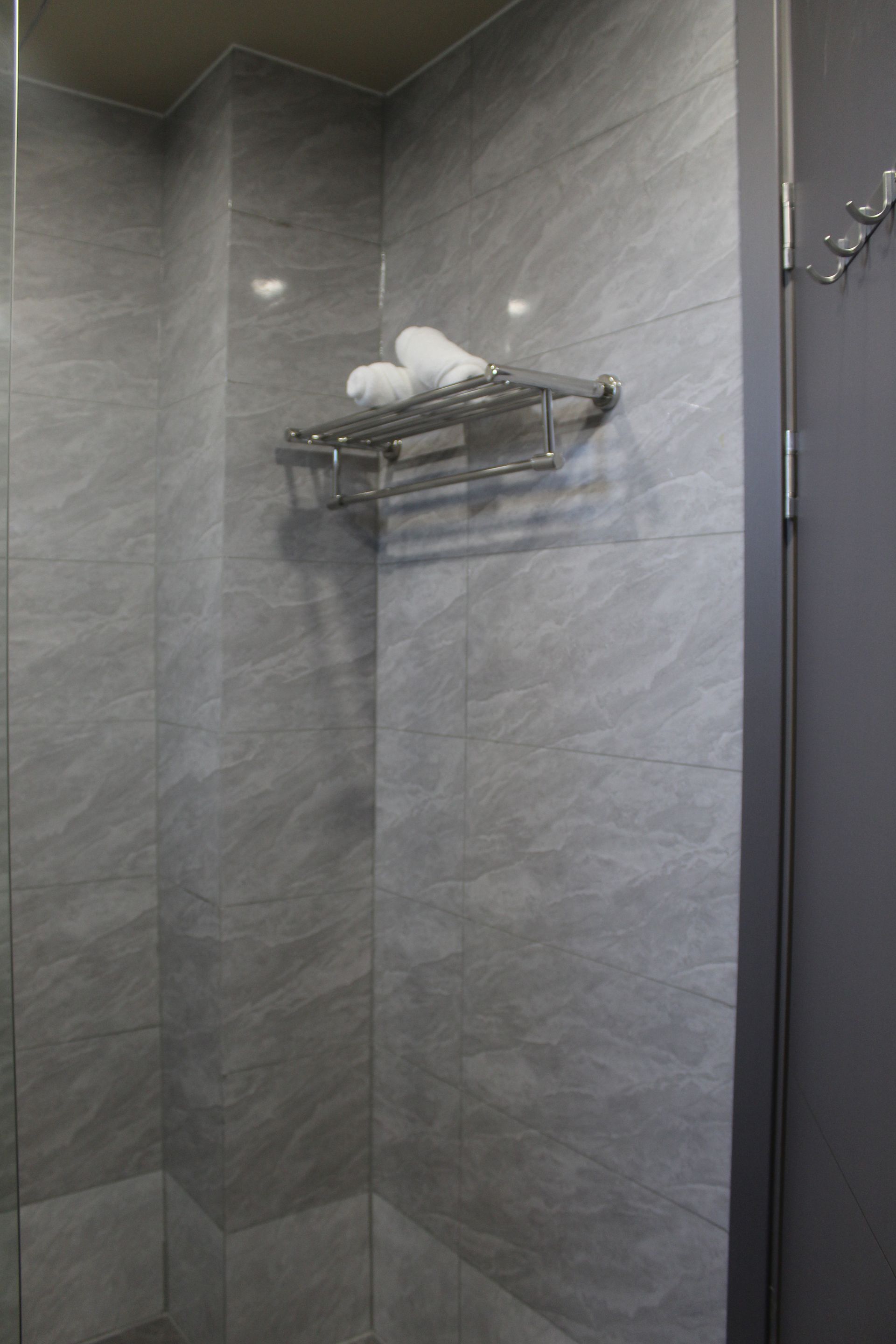 Gray-tiled shower with a towel rack holding two white towels. The door frame is visible on the right.