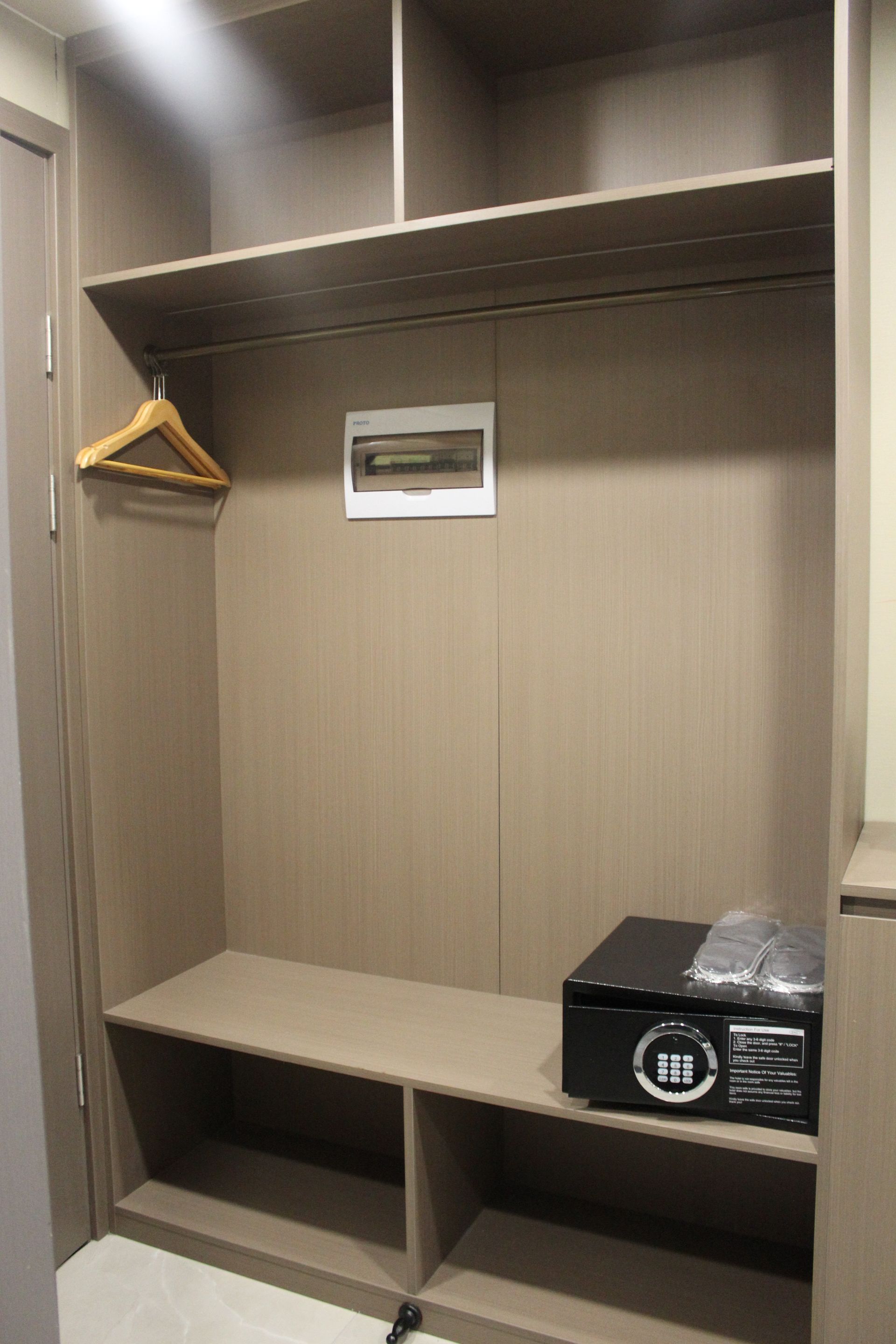 Built-in closet with shelves, a hanging rod, safe, and electrical panel; light brown wood.