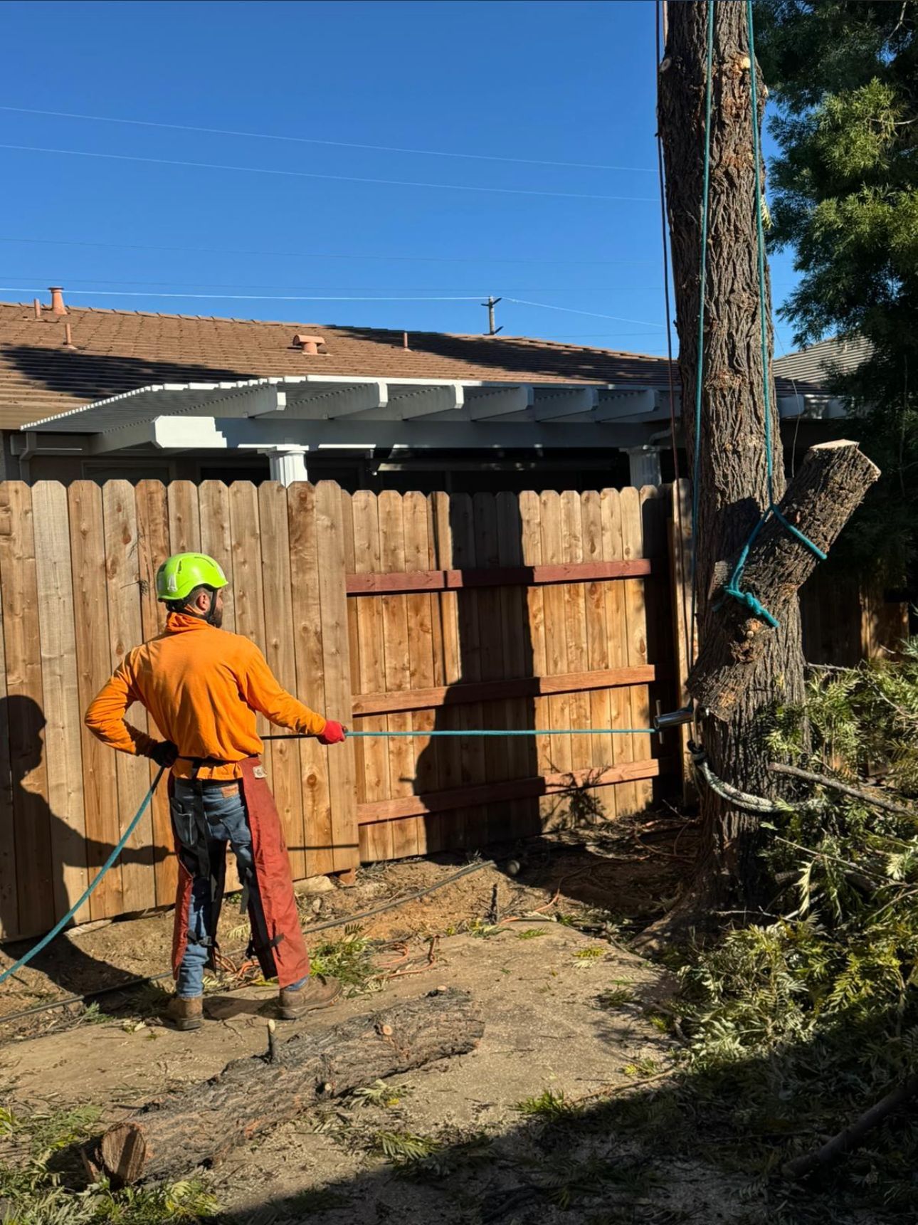 An orange tractor with a front-end loader sits on a lawn, next to a house and trash cans.