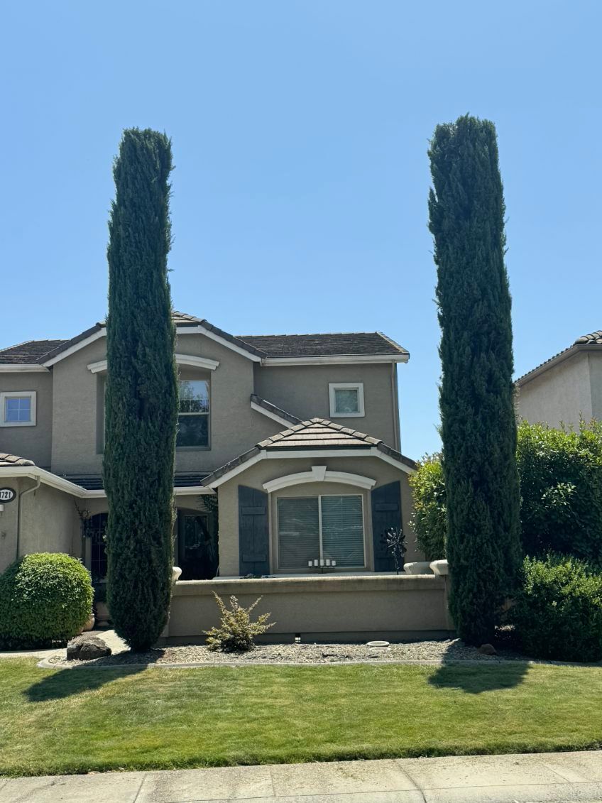Stone building with a dark roof and trees, a winding road, and a cloudy sky.