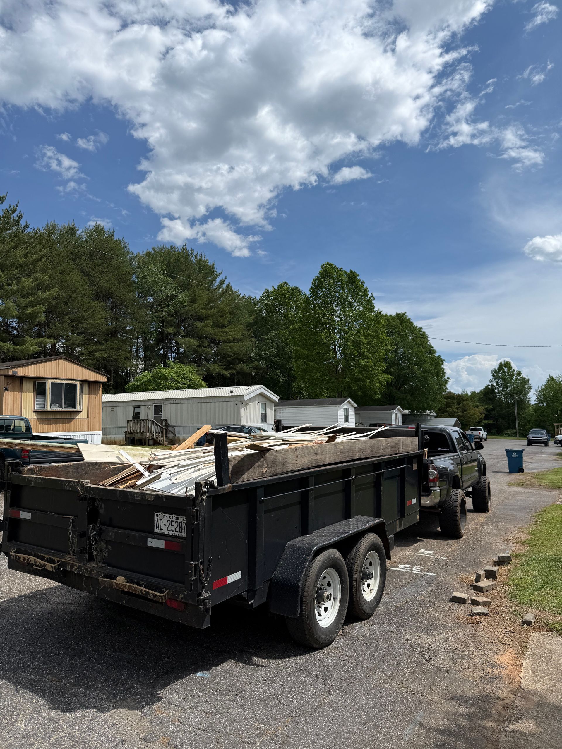 A dump truck with a trailer full of junk is parked on the side of the road.