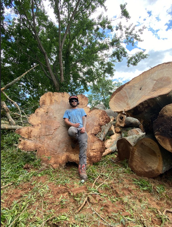 A man is sitting on a large tree stump in the woods.