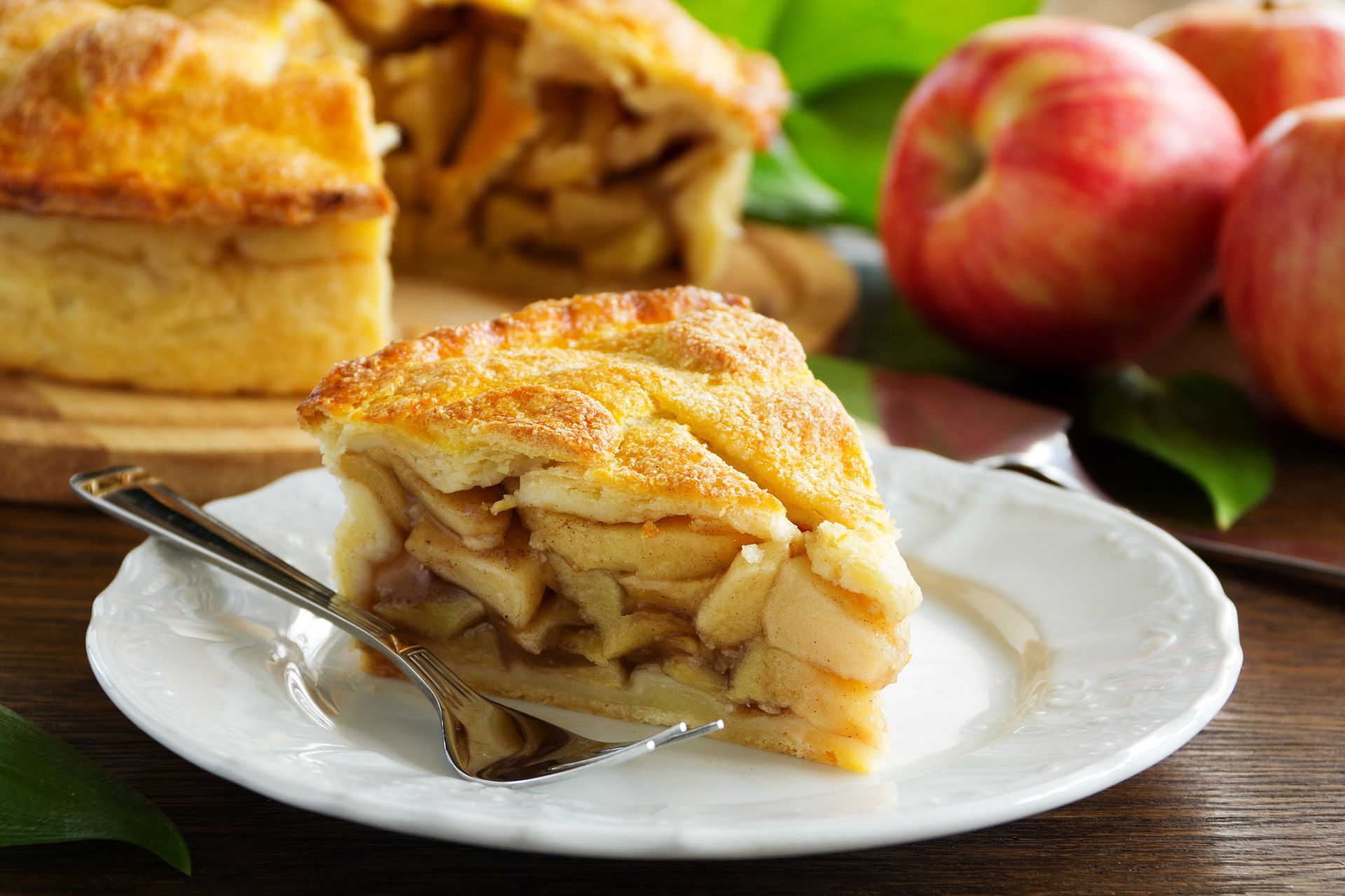 A slice of apple pie on a white plate with a fork.