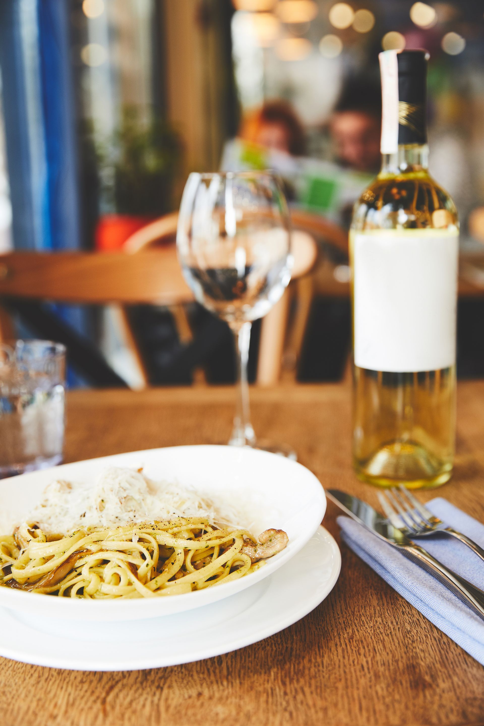 There is a bowl of pasta and a bottle of wine on the table.